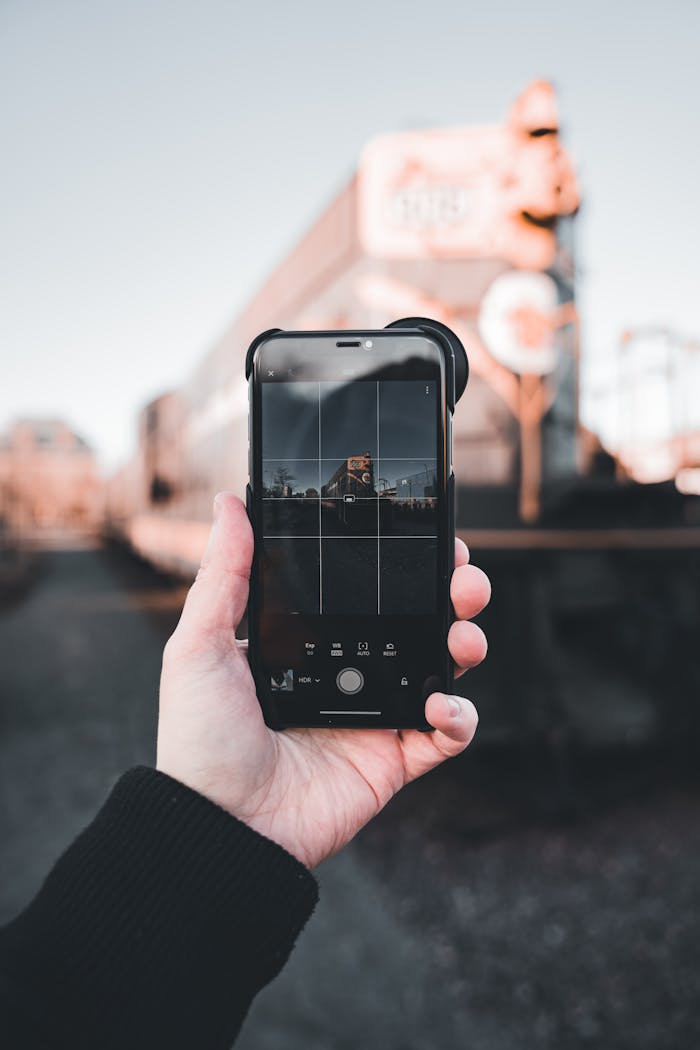 Close-up of a hand using a smartphone to photograph an urban scene with a blurred background.